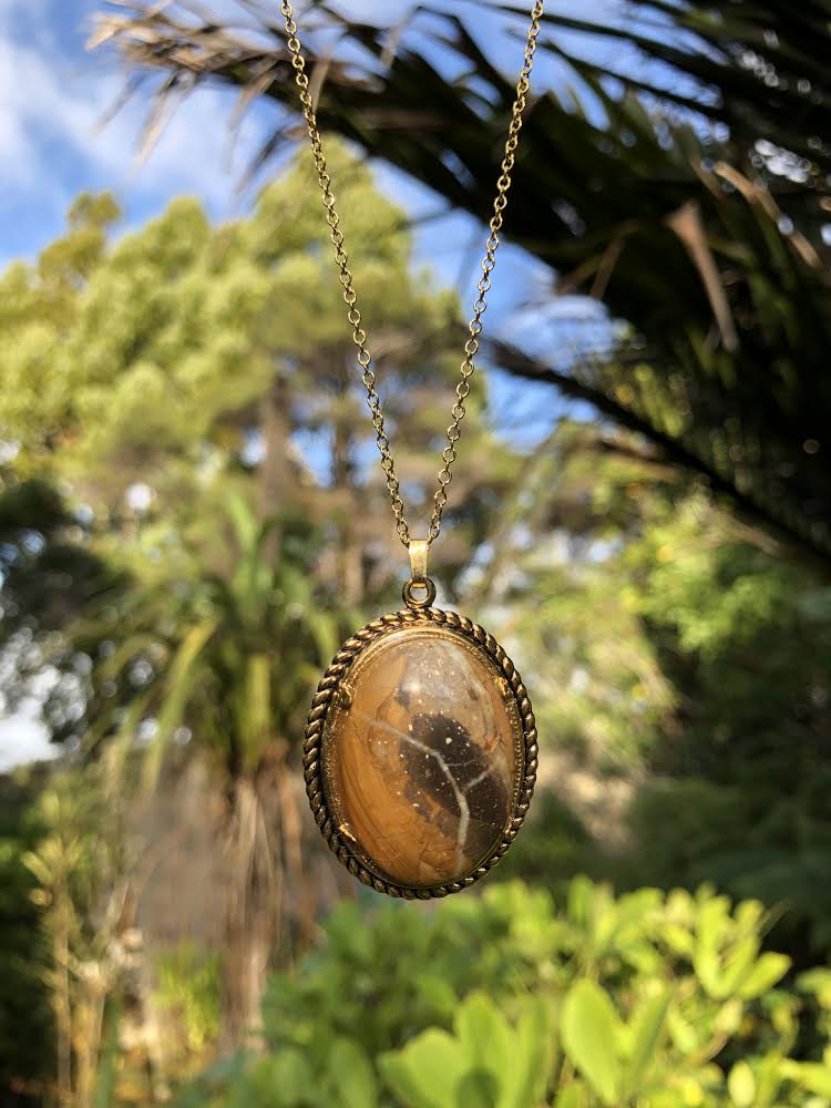 Necklace with natural petrified wood from Coromandel, New Zealand with browns and black and a white lightening bolt of chalcedony running through it, hand polished to a 30x22mm cabochon and set in a gold plated setting with 19 inch chain.