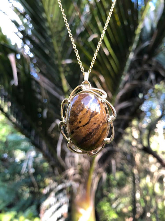 Necklace with natural petrified wood collected from the Manaia creek on the coromandel peninsula in New Zealand with striking brown and tan markings, hand polished to a 30x22mm cabochon and set in a gold plated setting with 19 inch chain.