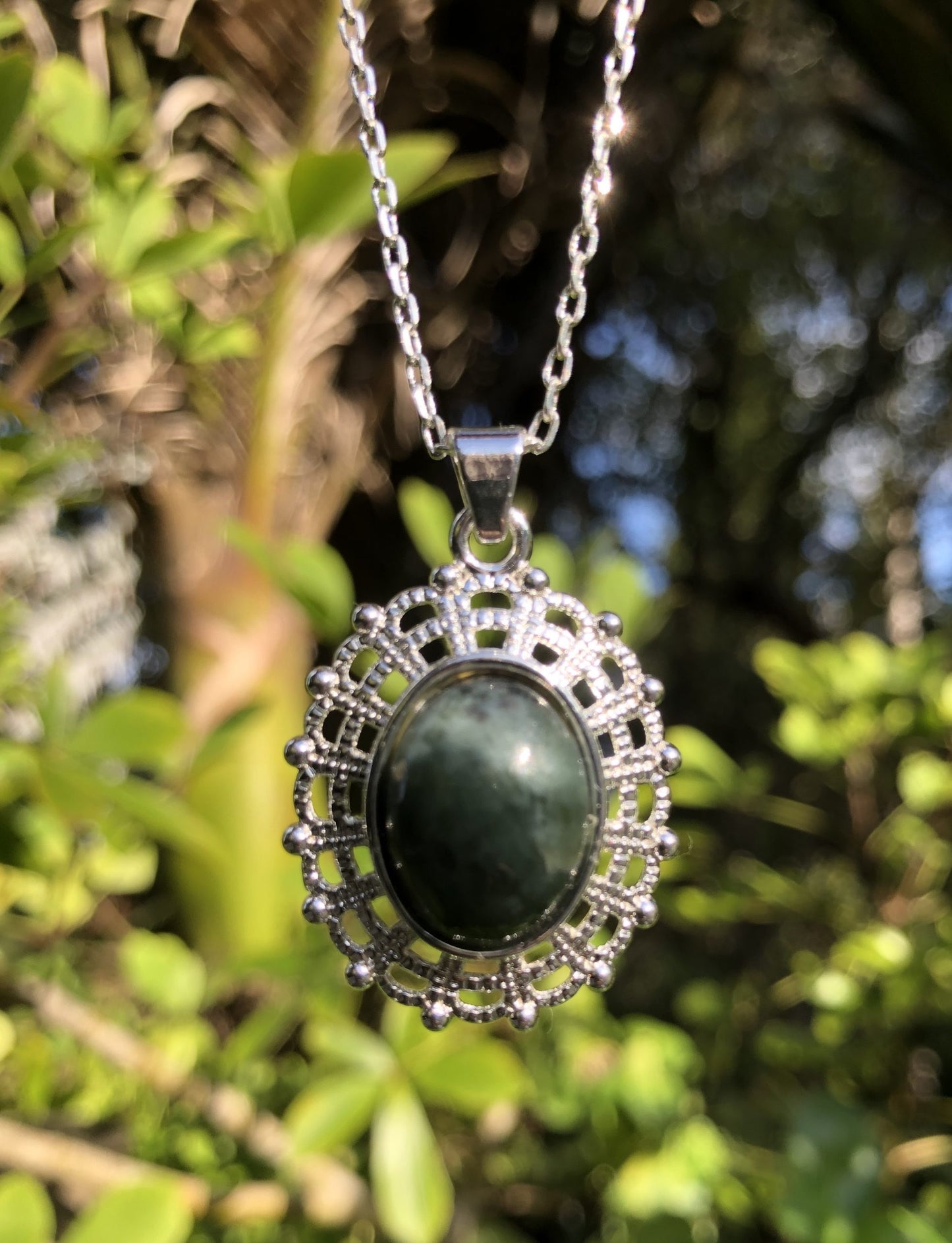 Necklace with New Zealand Pounamu (Greenstone, nephrite jade), dark green with mysterious markings, hand polished to an 18x13mm cabochon and mounted in a silver plated setting with 19 inch chain.