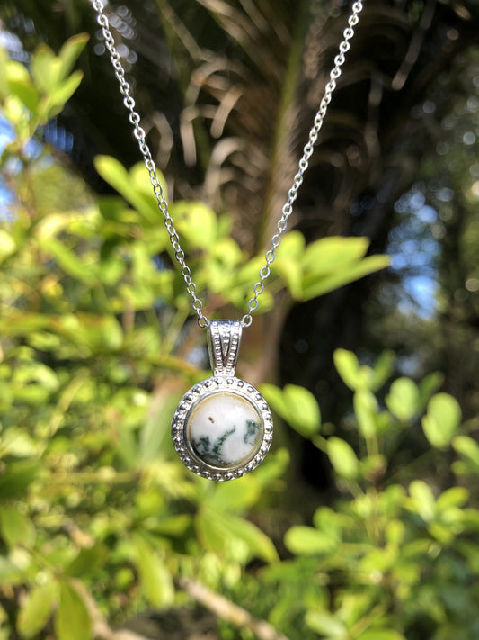 Necklace with natural Tree-Agate showing dark green moss on a bright white background, hand polished to a 10mm round cabochon and set in a silver plated setting with 19 inch chain, on bush