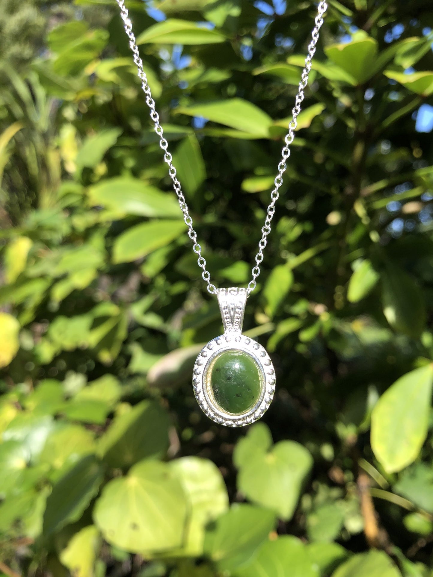 Necklace with New Zealand Pounamu (Greenstone, nephrite jade), bright green Kawakawa jade with subtle black marks, hand polished to an 12x10mm cabochon and mounted in a silver plated setting with 19 inch chain.