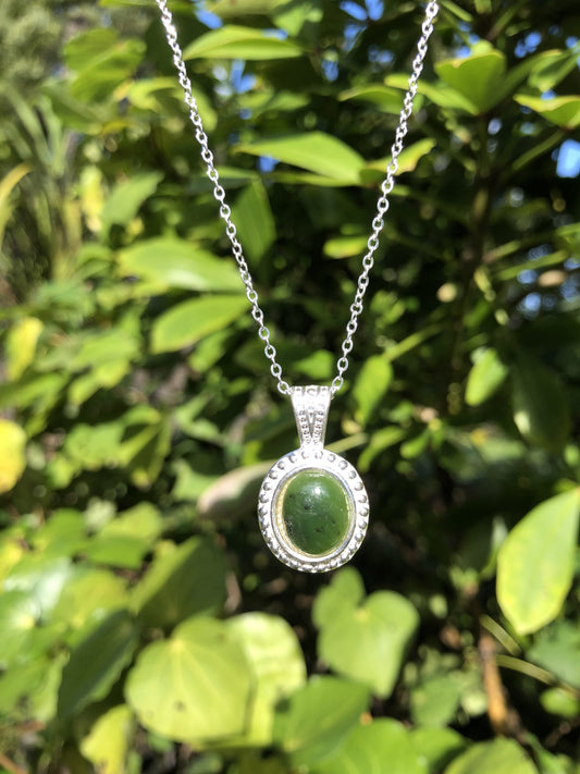 Necklace with New Zealand Pounamu (Greenstone, nephrite jade), bright green Kawakawa jade with subtle black marks, hand polished to an 12x10mm cabochon and mounted in a silver plated setting with 19 inch chain.