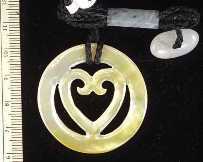 Necklace of hand carved and polished mother of pearl with a koru-heart in a torus, tied with a hand braided string with white quartz toggle. This piece is creamy white with rainbows of pearlescent pinks, greens, blues and yellows shimmering through - on black