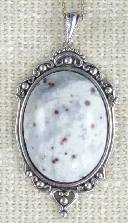 Necklace of hand carved and polished mother of pearl with a koru-heart in a torus, tied with a hand braided string with white quartz toggle. This piece is creamy white with rainbows of pearlescent pinks, greens, blues and yellows shimmering through.