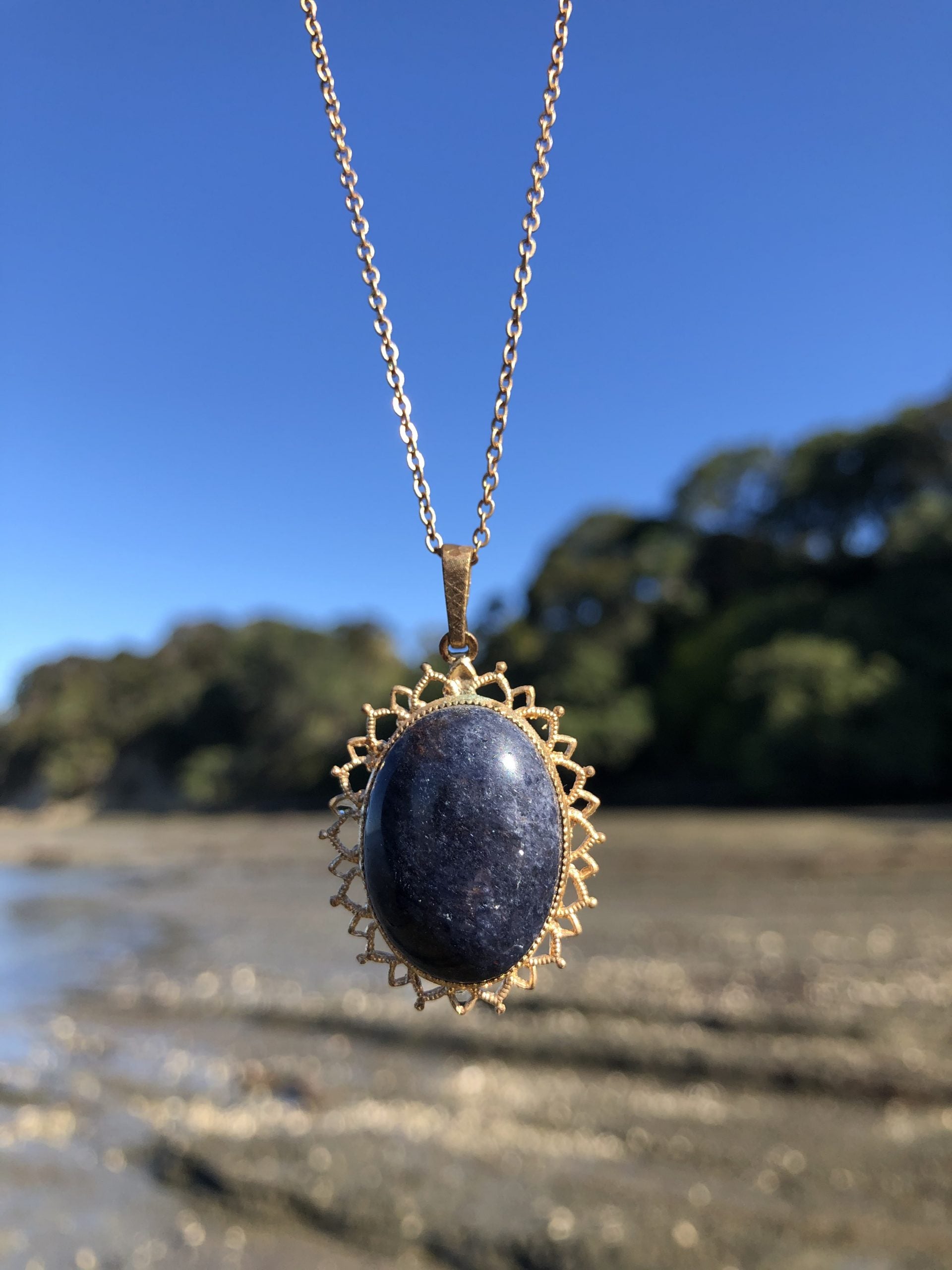 Necklace with natural blue aventurine, hand polished to a 25x18mm cabochon and set in a gold plated setting with 19 inch chain, on beach
