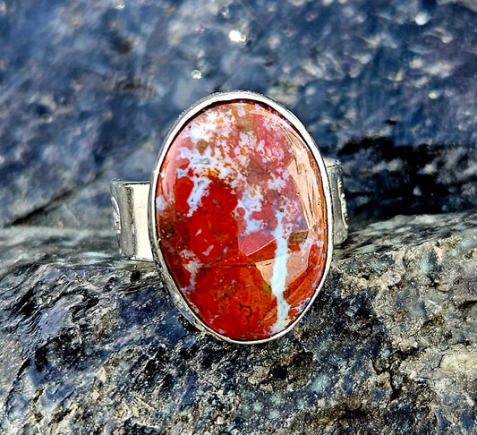 A vibrant red New Zealand jasper with striking lines of white quartz running through it, hand cut and polished to an 18x13mm cabochon and set in a sterling silver, adjustable ring, front.