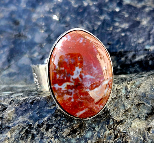 A vibrant red New Zealand jasper with striking lines of white quartz running through it, hand cut and polished to an 18x13mm cabochon and set in a sterling silver, adjustable ring, front.