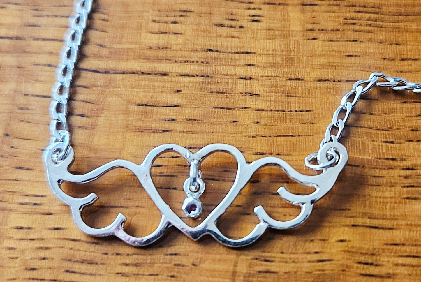 Small (40mm wide) Heart-Wing pendant with a ruby charm, all in solid sterling silver and a solid sterling silver heavy chain on wood.