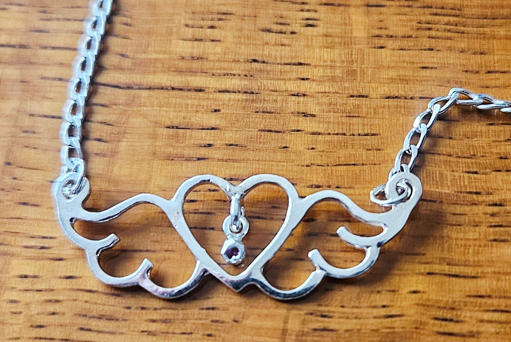 Small (40mm wide) Heart-Wing pendant with a ruby charm, all in solid sterling silver and a solid sterling silver heavy chain on wood.