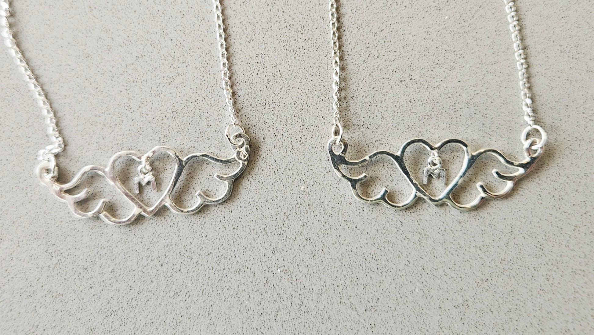 Small (40mm wide) Heart-Wing pendant with a letter "M" charm, for Mother, all in solid sterling silver and a solid sterling silver chain. This is a perfect Mother's Day gift, 2 on gray.