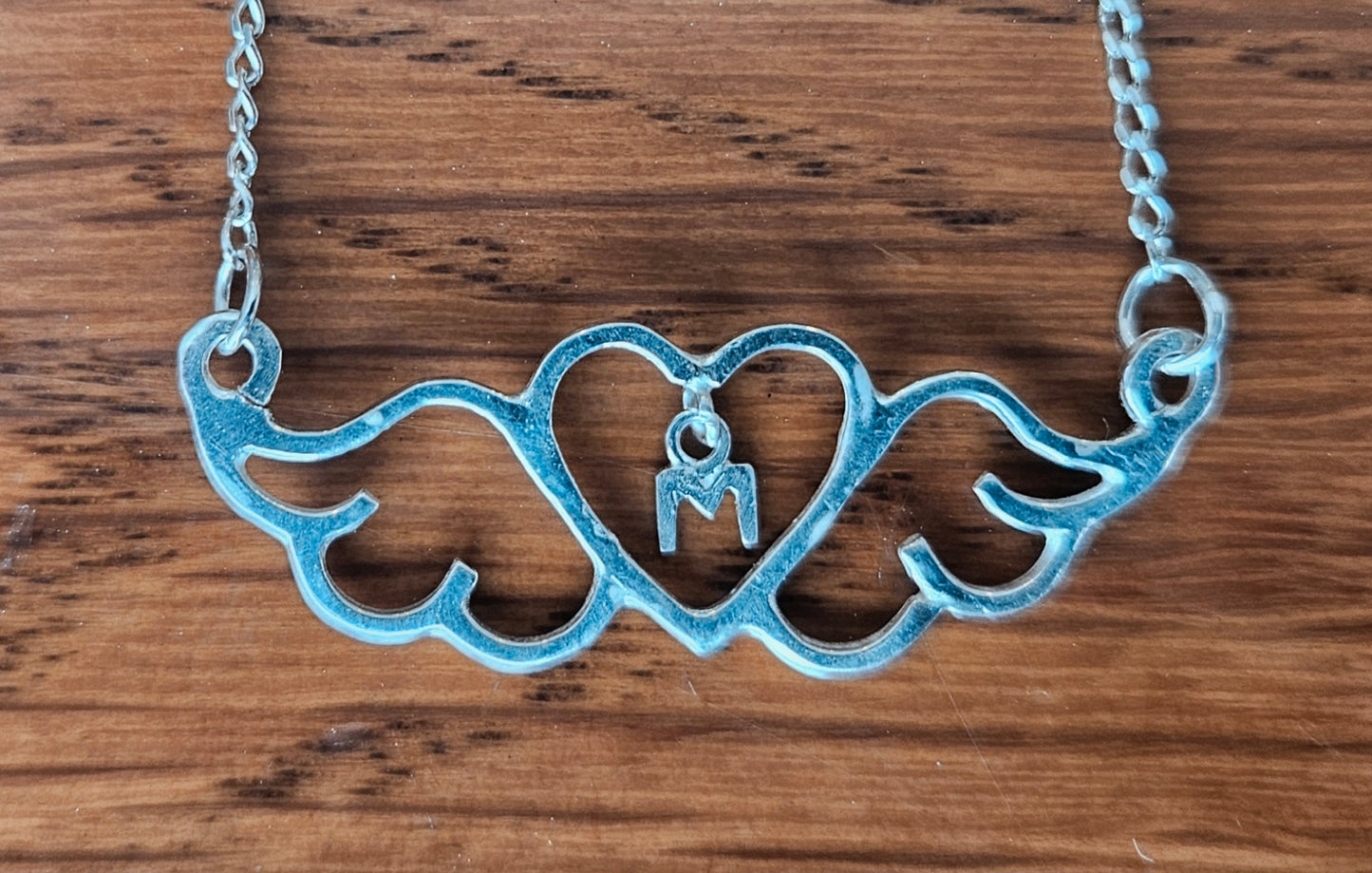 Silver necklace with a heart and wing design on a wooden surface