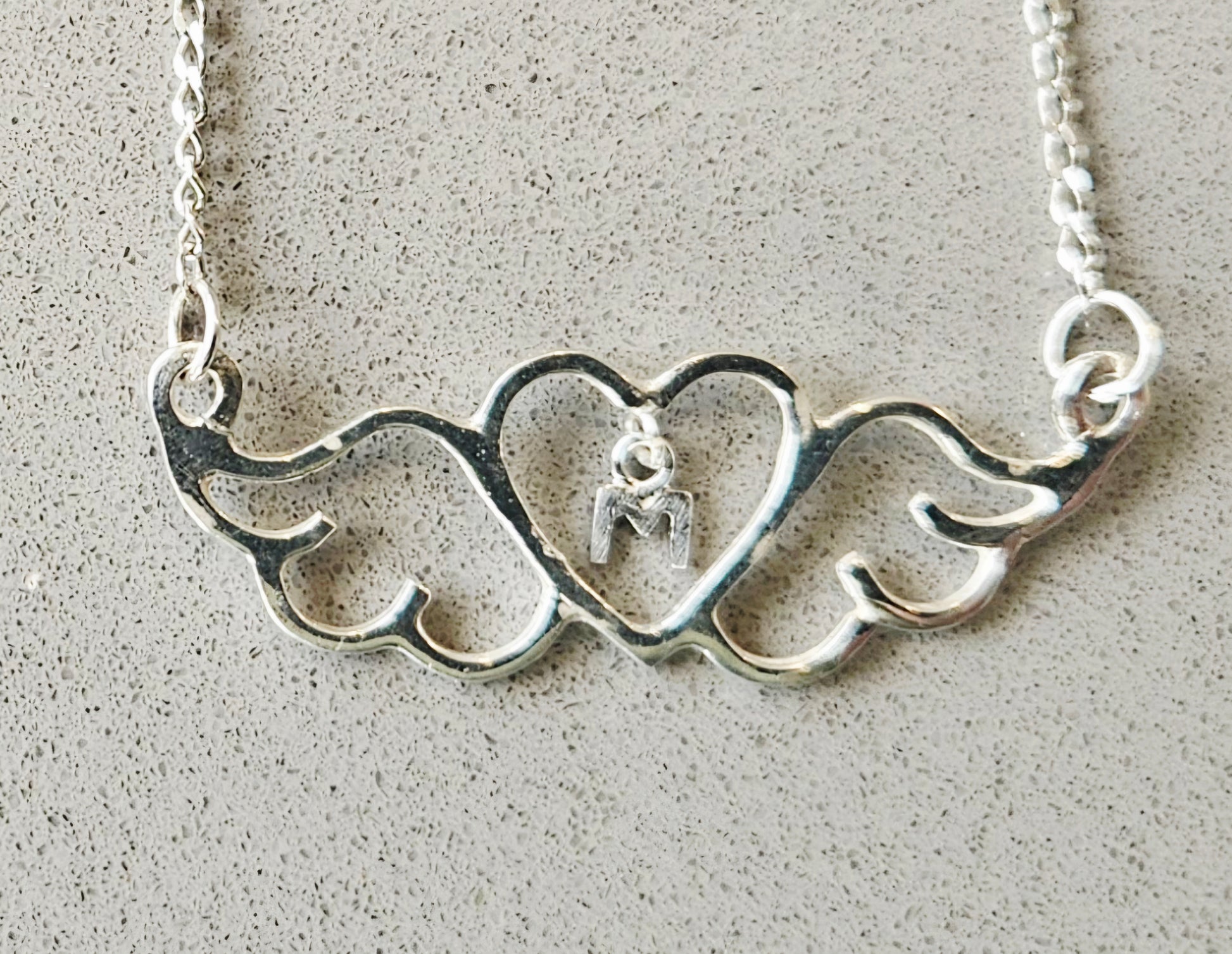 Silver necklace with heart and wing design on a textured surface