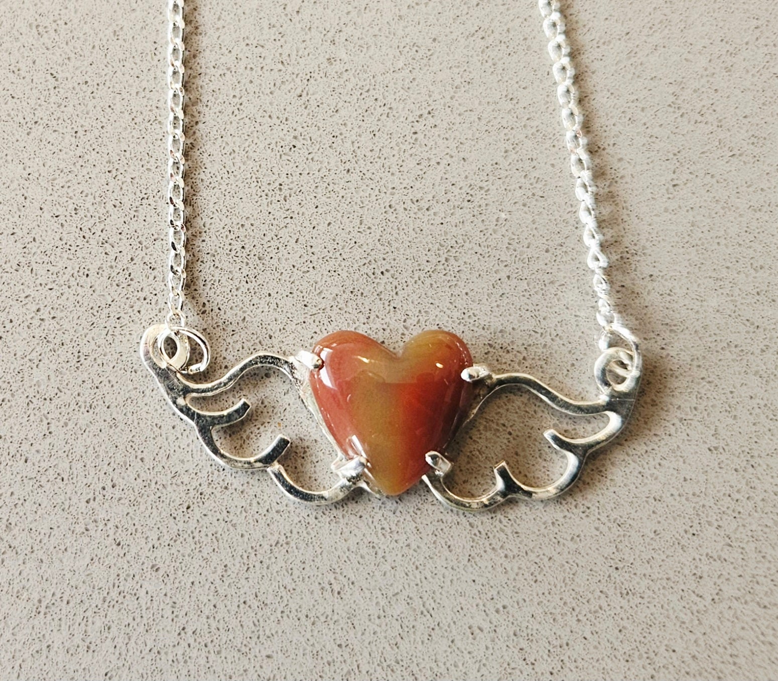 Small (40mm wide) Heart-Wing pendant with a 13x13mm heart cabochon, hand cut and polished from natural New Zealand jasper, all in solid sterling silver and a solid sterling silver chain on gray background.