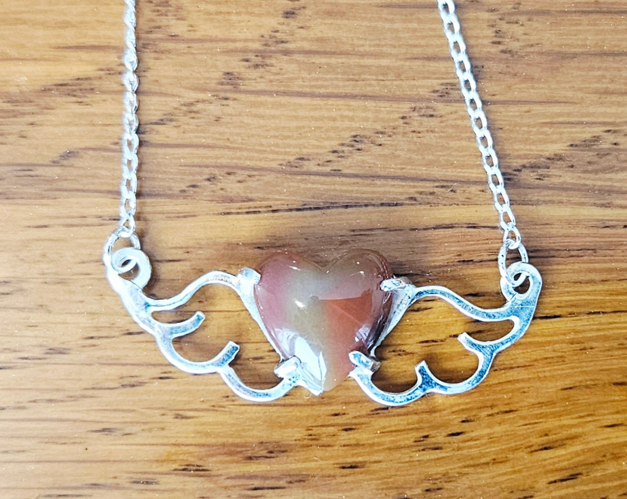 Small (40mm wide) Heart-Wing pendant with a 13x13mm heart cabochon, hand cut and polished from natural New Zealand jasper, all in solid sterling silver and a solid sterling silver chain, on wood.