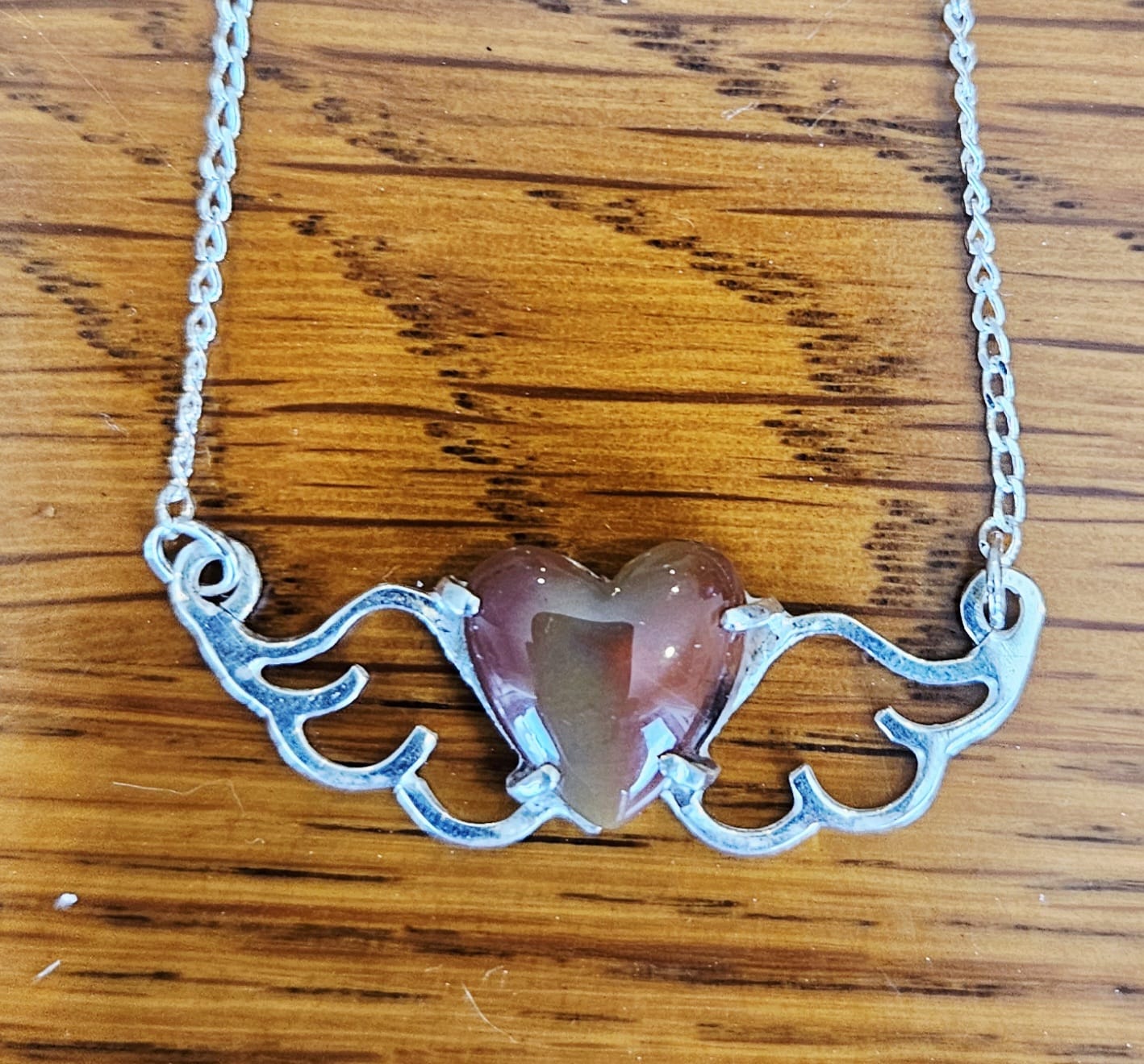Small (40mm wide) Heart-Wing pendant with a 13x13mm heart cabochon, hand cut and polished from natural New Zealand jasper, all in solid sterling silver and a solid sterling silver chain, on wood, darker.